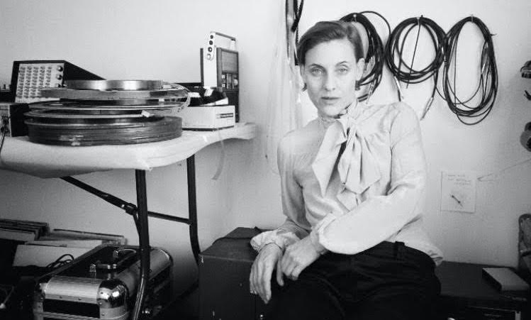 A woman in a blouse sits in front of a table covered in audio equipment.