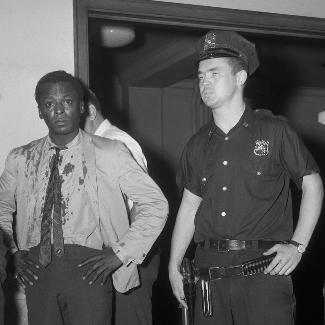 Miles Davis stands in a bloodied shirt next to a member of the NYPD.