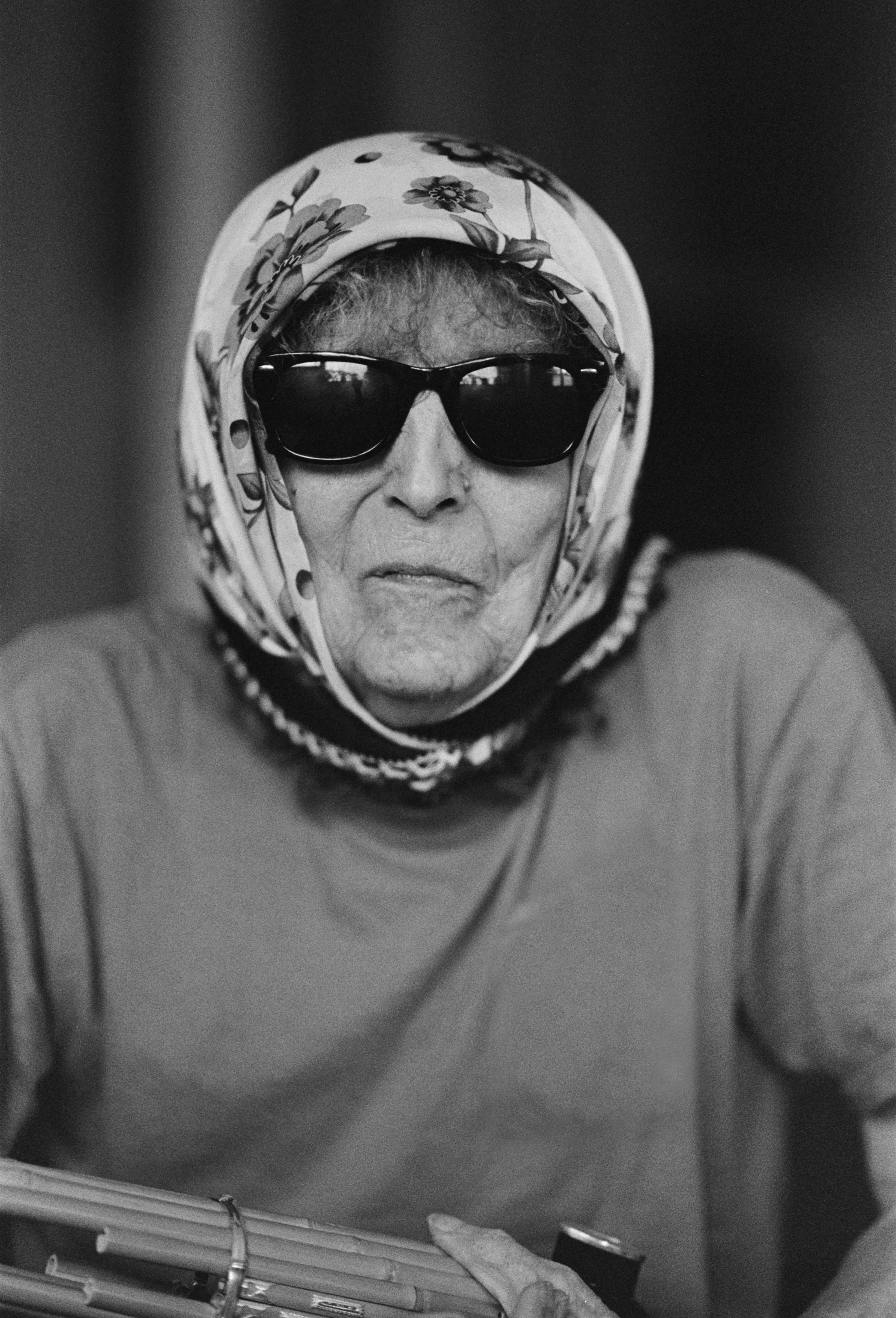 Catherine Christer Hennix wears a headscarf, black sunglasses, and a t shirt and holds a sho.